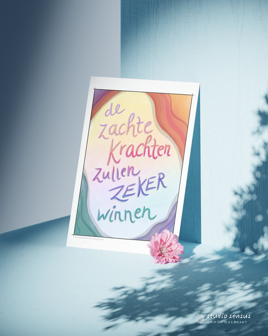 Poster Met de tekst 'De zachte krachten zullen zeker winnen', deze staat tegen een muur in zachtblauw, waarop schaduw van een boom te zien is. Voor de poster ligt een roze bloem.