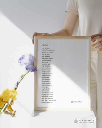 Een ingelijste poster met het gedicht 'Mijn kind', geschreven door Michèlle van Vlerken. Mijn kind. Blijf alsjeblieft - jouw twinkelverhalen, dromen en dwalen - wijs en naïef - blijf alsjeblieft - zoekend en wetend - niets vergetend - alles kwijt - woede en spijt - blijf alsjeblieft - jouw ratelvragen - droomverslagen - vlindervoelend - naast me woelend - warme wangen - onbevangen - blijf alsjeblieft - zuiverziend en wonderwegend - plassen stampend in de regen - ongeleid wild - dauw en zilt