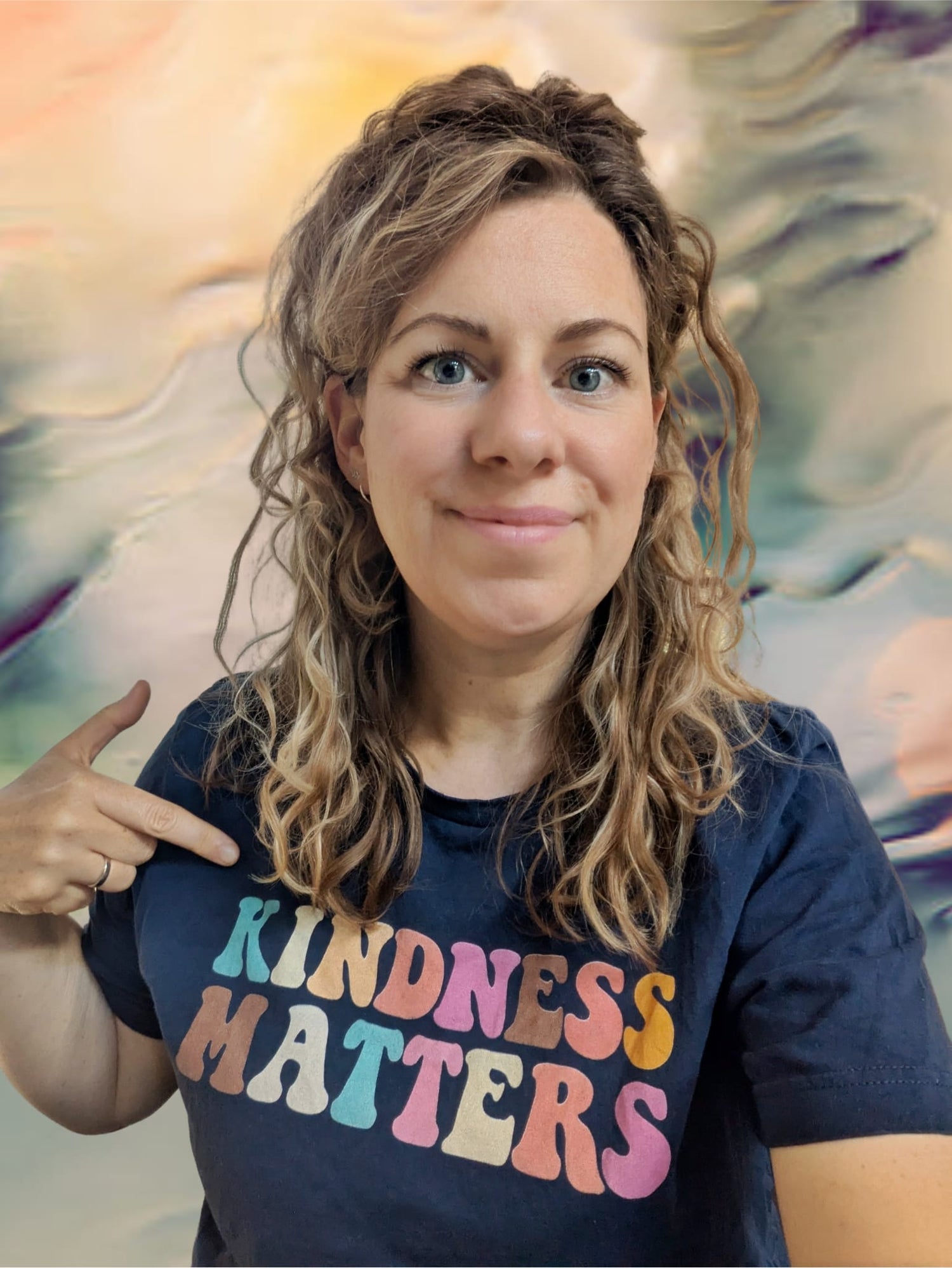 Portret van Michèlle. Ze wijst naar haar t-shirt, waar kindness matters op staat in regenboogkleuren